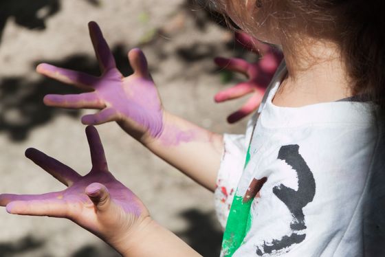 Foto: Ein Kind schaut auf seine mit Farbe verschmierten Hände.