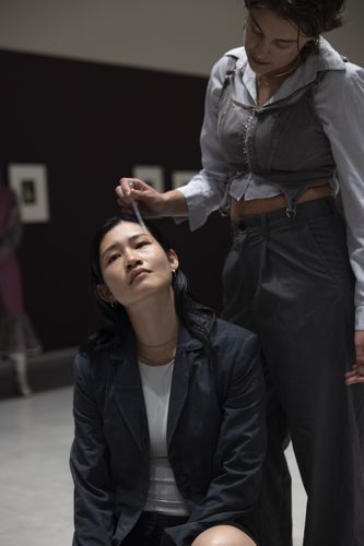 Chihiro Araki and Deva Schubert during the performance ‘Glitch Choir’ at the Berlinische Galerie Photo: Deva Schubert stands behind Chihiro Araki, who is sitting on the floor, dripping tears onto her cheek with a pipette.