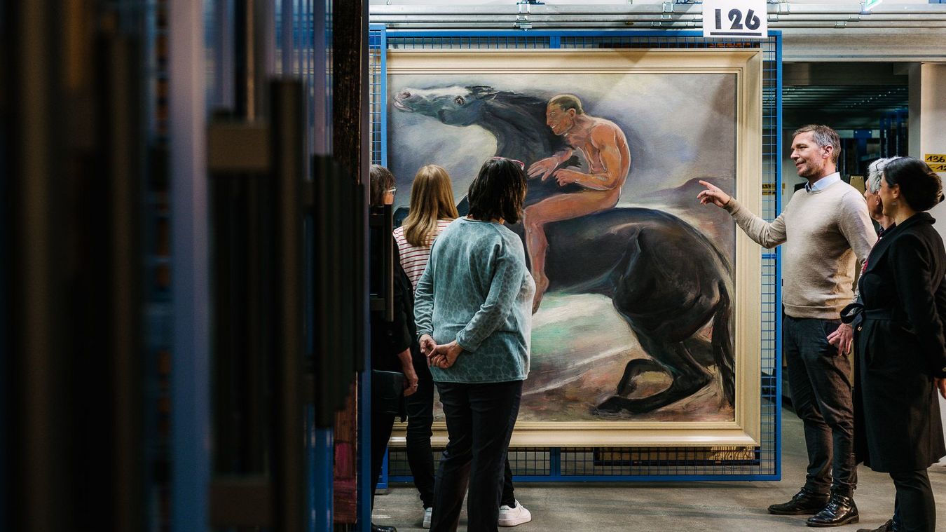 Foto: Besucher*innen während einer Führung im Museumsdepot. Sie betrachten ein Kunstwerk an einem Ziehgitter.
