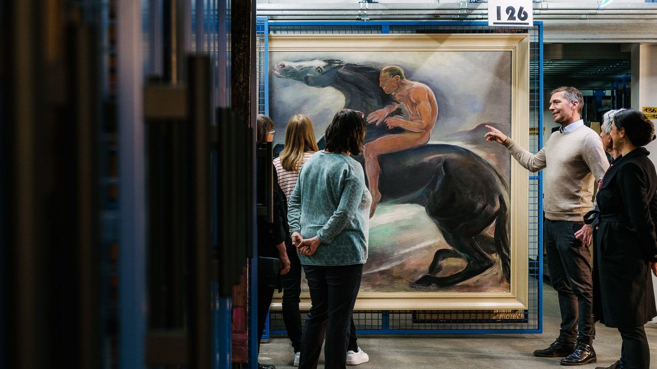 Photo: Visitors during a guided tour of the museum depot. They are looking at a work of art on a grid.