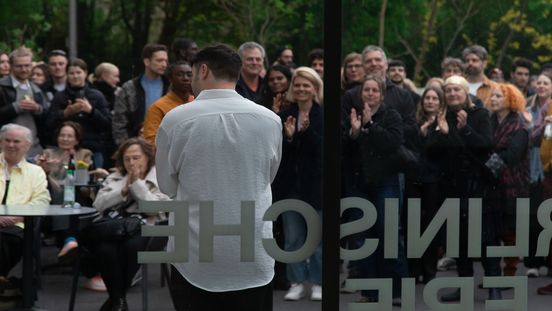 Der Künstler Daniel Hölzl spricht vor einem applaudierenden Publikum im Freien vor der Berlinischen Galerie.