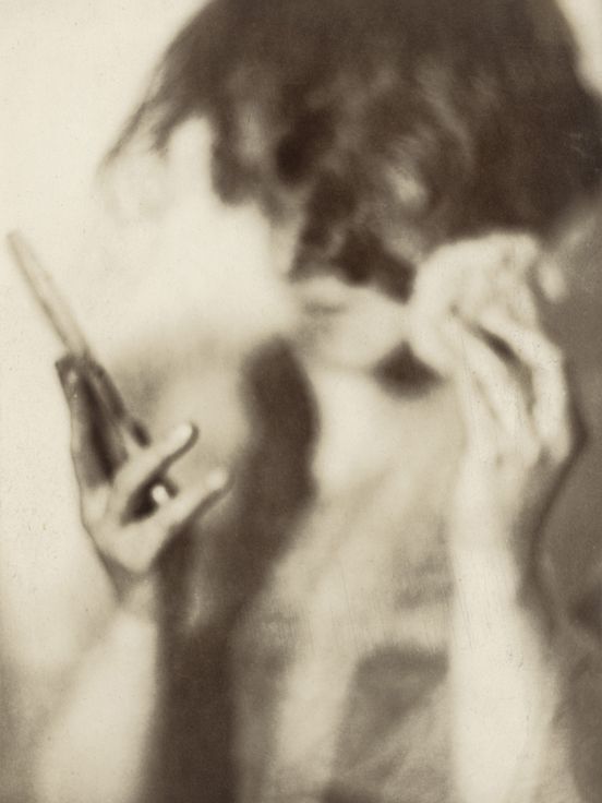 Sepia photograph: A female figure looks sideways at a small mirror, which she holds in her right hand. In her left hand she holds a small powder puff.