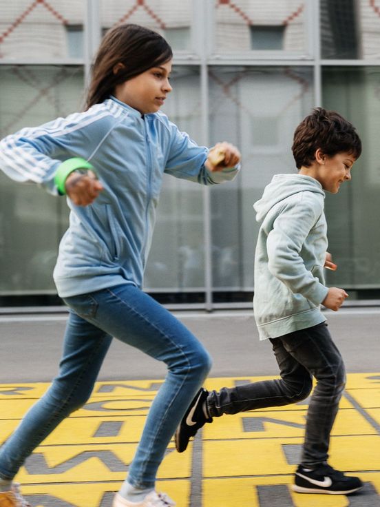 Photo: Three children run across a piece of floor art in front of the museum: grey letters on a yellow background.