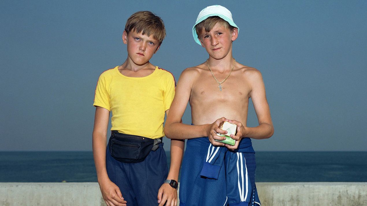 Foto: Zwei Jungen stehen vor einer niedrigen Ballustrade aus Beton, im Hintergrund ist das Meer zu sehen. Beide tragen Sportkleidung und blicken direkt in die Kamera.