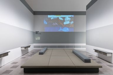 Photo: In the centre of a room is a large upholstered seating and reclining area. Sideboards on the walls to the right and left. An image is projected onto the centre wall.