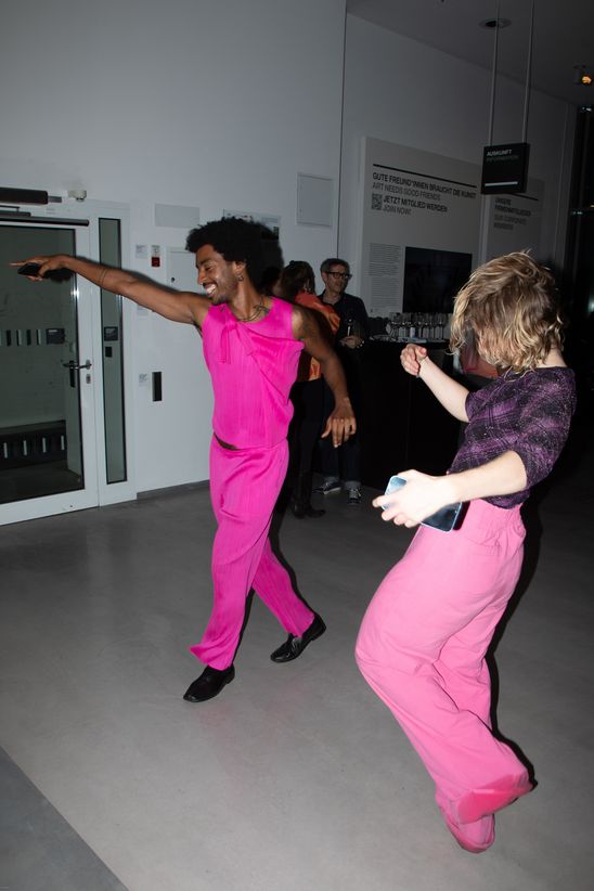 Foto: Zwei Personen mit pinken bzw. teilweise pinkfarbenen Outfits tanzen im Foyer der Berlinischen Galerie.