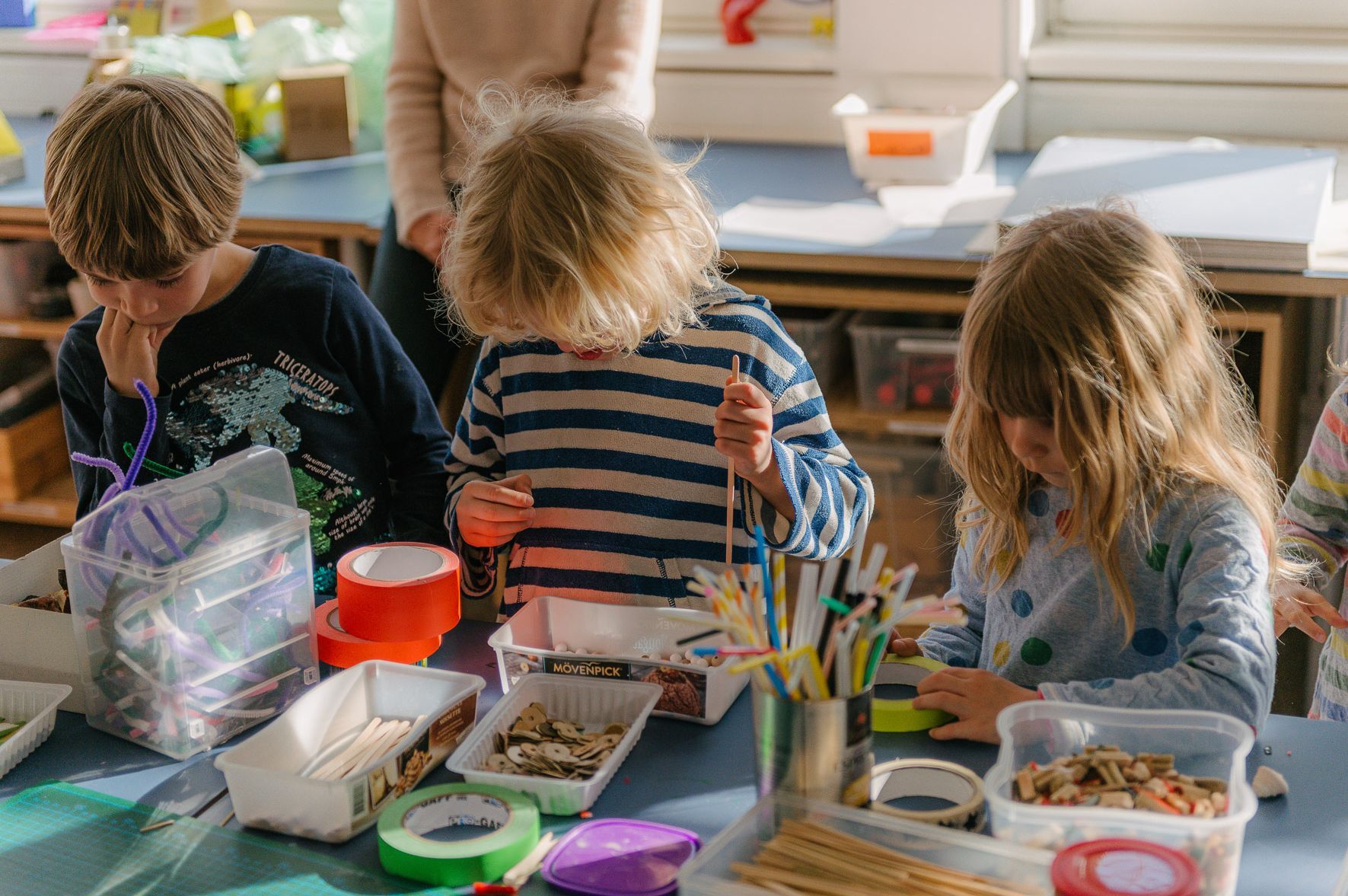 Foto: Drei Kinder spielen mit Bastelmaterialien auf dem Tisch vor ihnen.