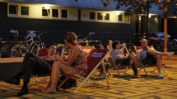 Am Abend sitzen mehrere Personen entspannt auf Liegestühlen auf dem Buchstabenfeld vor der Berlinischen Galerie.