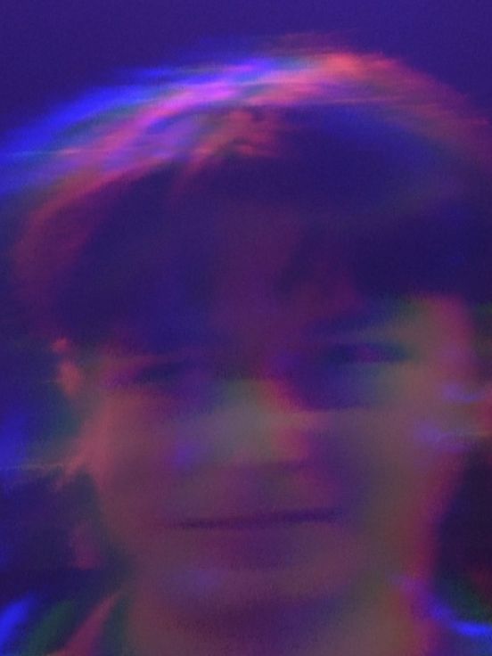 Filmstill: Das Filmstill zeigt die verschwommenen Gesichter von zwei Personen, die in lila Licht getaucht sind.