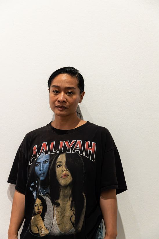 Porträtfoto von Stephanie Comilang in einem schwarzen Tshirt mit farbigem Print und Schriftzug vor einer weißen Wand.