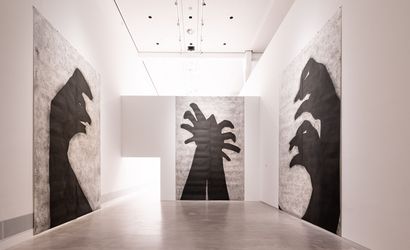 Foto: Blick in einem menschenleeren Ausstellungsraum. An den Wänden hängen großflächige Arbeiten, die Schattenfiguren in schwarz auf weiß-grauem Hintergrund zeigen.