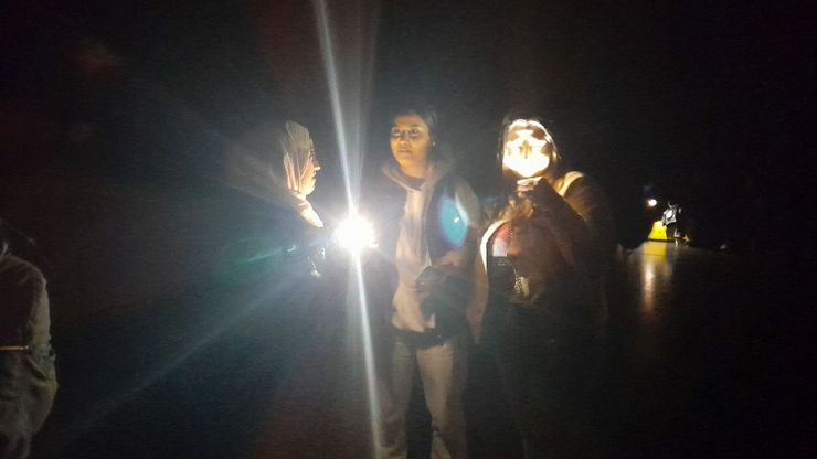 Drei Schüler*innen stehen in einem dunklen Raum und leuchten mit einer Taschenlampe.