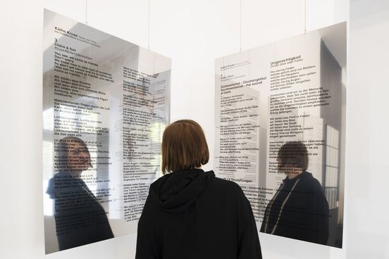 Photo: Käthe Kruse stands with her back to the camera between two large mirrors printed with black text.