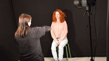Foto: In einem Raum mit schwarzen Wänden und Scheinwerfern fotografiert eine Person eine andere Person.