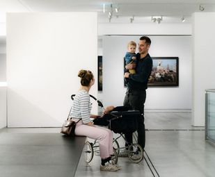 Photo: Two adult exhibition visitors with a small child in the Berlinische Galerie.