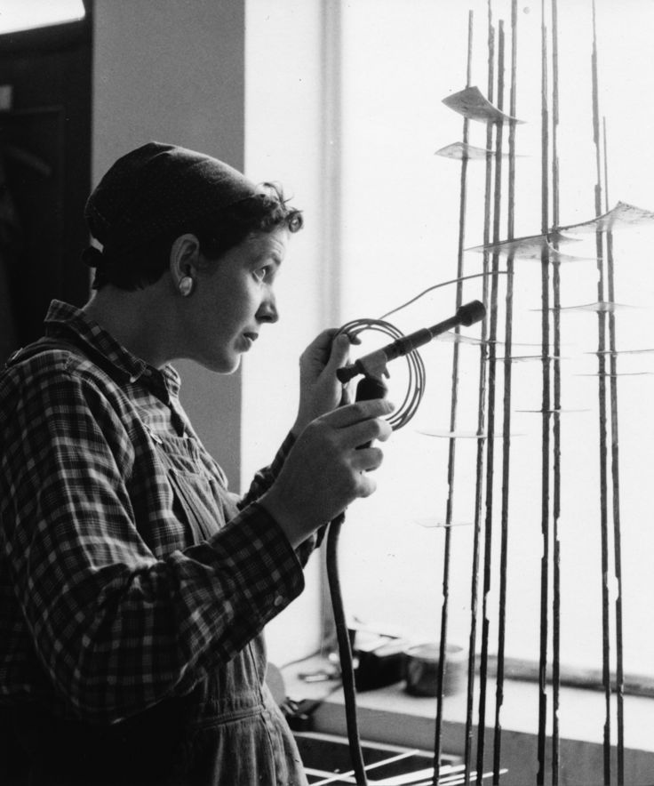 Brigitte Meier-Denninghoff, Munich 1957 Black and white photo: Side view of Brigitte Meier-Denninghoff working on one of her sculptures in front of a window with a soldering iron in her hand.
