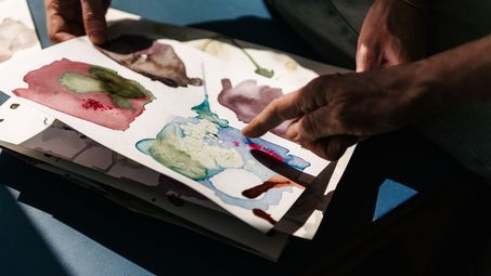 Photo: Several hands hold a painted picture and point to it.