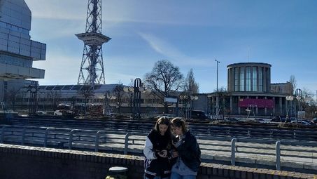 Zwei Schüler*innen schauen gemeinsam auf ein Tablet. Im Hintergrund teilweise die Außenfassade des ICC-Gebäudes zu erkennen.