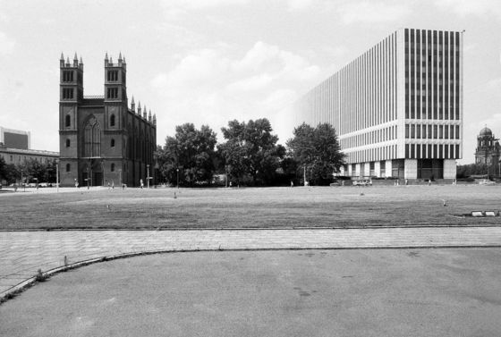 Weiter Platz mit Kirche, einem großen modernen Gebäudekomplex und Bäumen