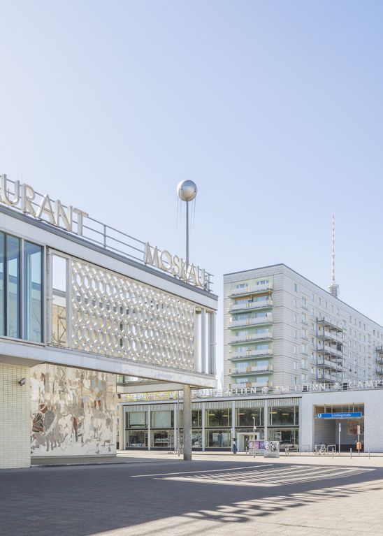 Ansicht des Café Moskau in Berlin mit dem Schriftzug „MOSKAU“, ornamentaler Fassade und umliegender DDR-Architektur unter blauem Himmel