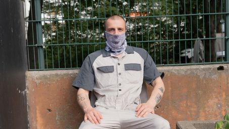 Foto: Eine Person posiert vor urbanem Hintergrund mit dem Loop-Schal, der wie eine Maske das halbe Gesicht verdeckt.