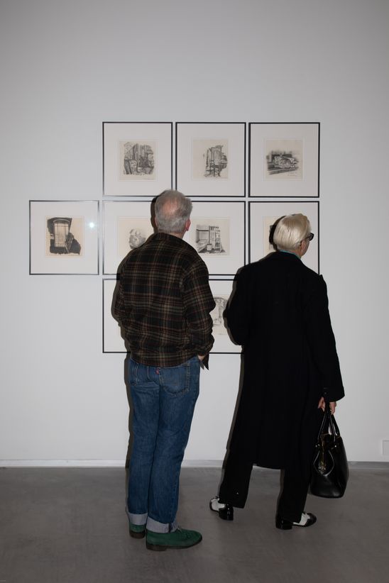 Foto: Rückenansicht von zwei Personen, die sich gerahmte Zeichnungen von Marc Brandenburg ansehen.