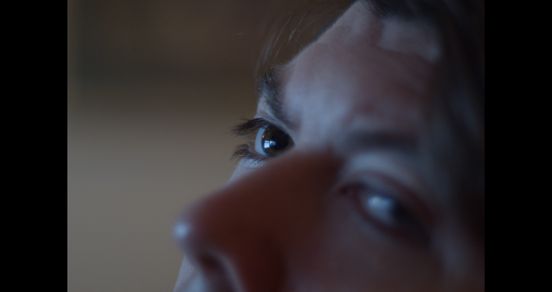 Film-Still: Nahaufnahme einer oberen Gesichtshälfte einer Person mit brauen Augen und braunem Haar.