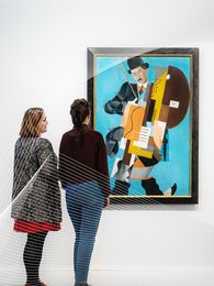 Foto: Mehrere Besucher*innen stehen und sitzen im Ausstellungsraum und betrachten Kunstwerke.