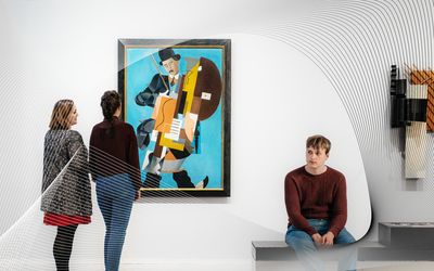 Foto: Mehrere Besucher*innen stehen und sitzen im Ausstellungsraum und betrachten Kunstwerke.