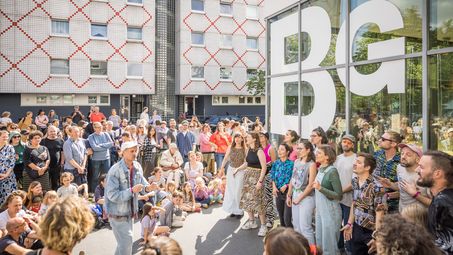 Foto: Die Mitglieder des Kiez Chors stehen in einem Halbkreis vor der Berlinischen Galerie und singen. Sie sind umgeben von viel Publikum.