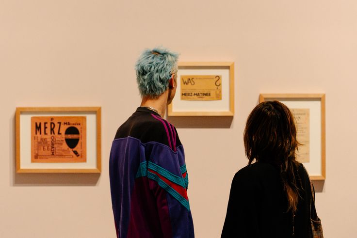 Foto: Rückenansicht von zwei Personen, die vor drei gerahmten Werken von Raoul Hausmanns stehen.