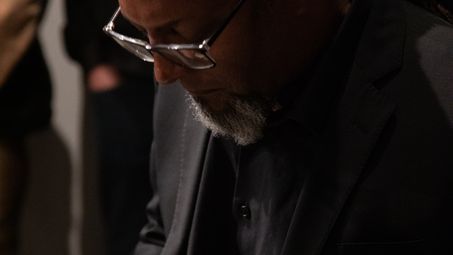 Close-up of Eliot Douglas in a black suit and glasses at the grand piano.