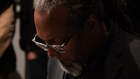 Close-up of Eliot Douglas in a black suit and glasses at the grand piano.