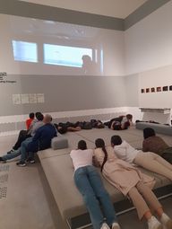 Die Klasse liegt auf dem Couchmöbel im Vermittlungsraum der Berlinischen Galerie und schaut nach oben an die Wand, auf die gerade ihre Videoarbeiten projiziert werden.