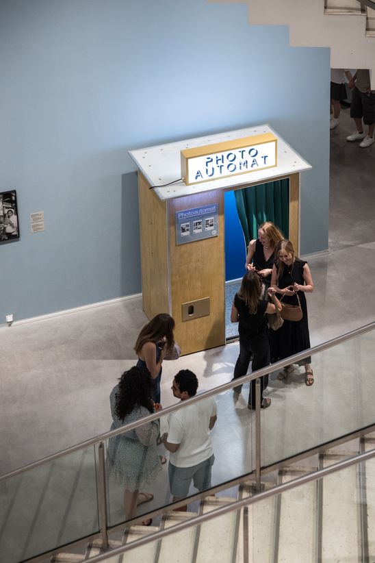 Foto: Einige Personen stehen vor einem hölzernen Fotoautomaten im Ausstellungsraum.