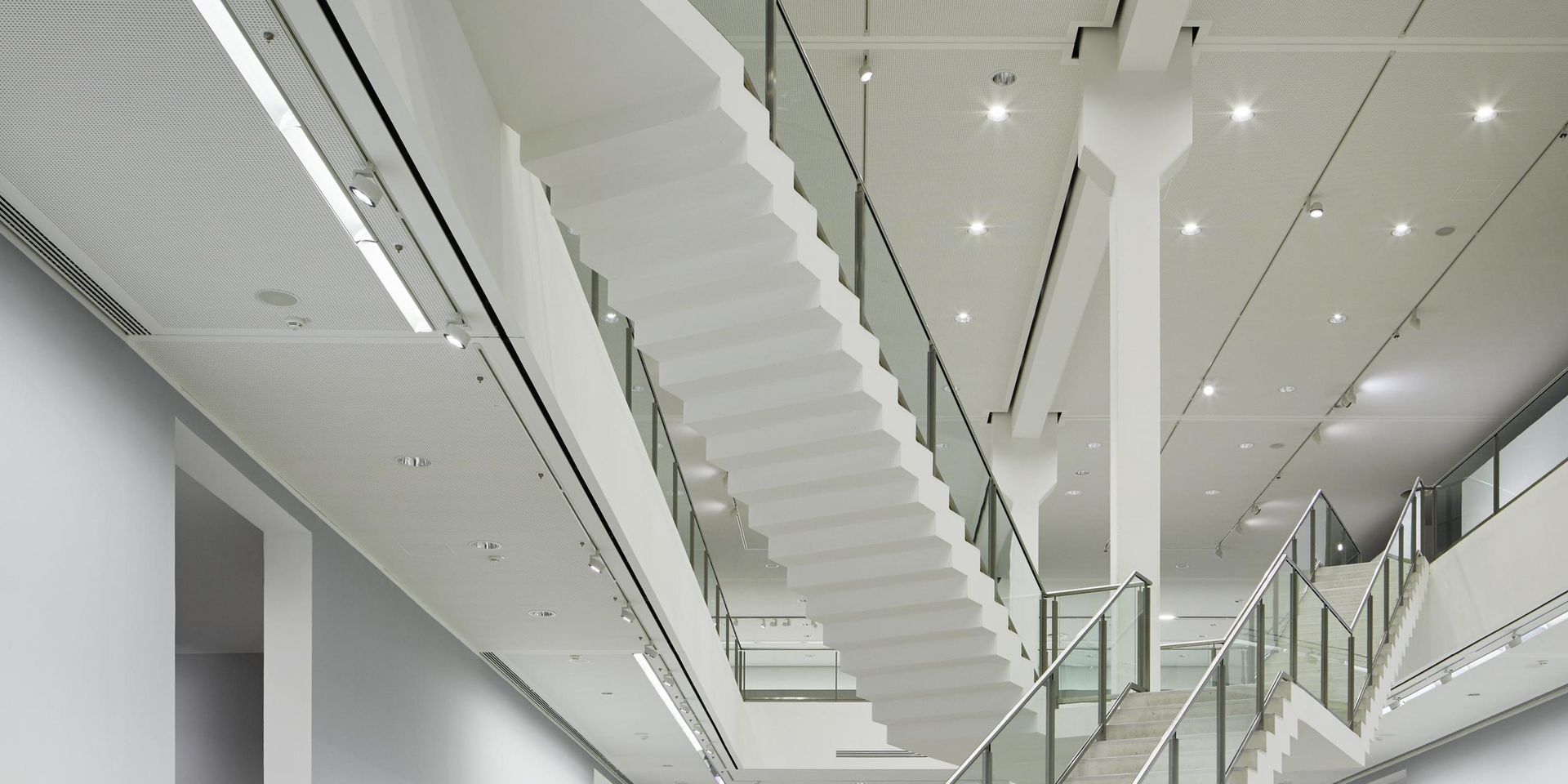 Photo: Two-storey exhibition space with artworks on the walls, two intersecting staircases in the middle.
