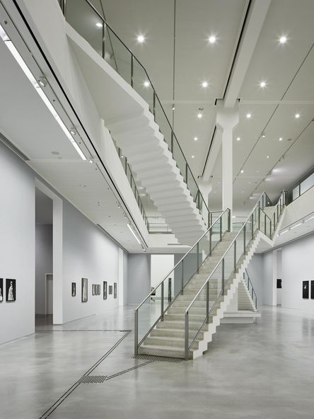 Photo: Two-storey exhibition space with artworks on the walls, two intersecting staircases in the middle.