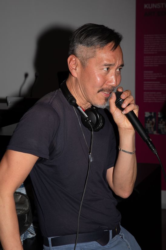 Foto: Seitlicher Blick auf Daniel Wang mit Mikrofon in der Hand am DJ-Pult.