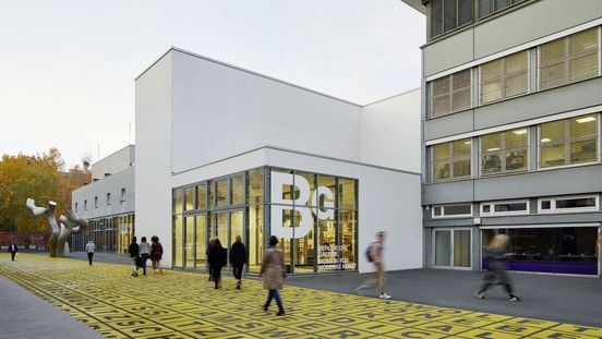 Foto: Gebäude mit Flachdach und Glasfront, auf der das Logo der Berlinischen Galerie abgebildet ist. Davor Menschen auf einem Platz mit Metallskulptur und Bodenkunstwerk.