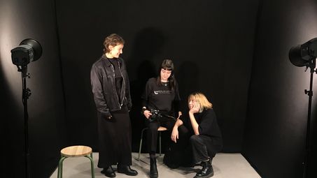 Foto: Drei junge Frauen in einem Raum mit schwarzen Wänden und Scheinwerfern.