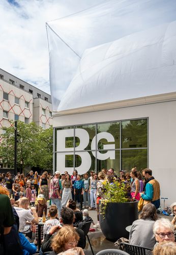 Concert by Projekt Kiezchor Photo: A group of colourfully dressed people stand in a semi-circle in front of the Berlinische Galerie and sing.
