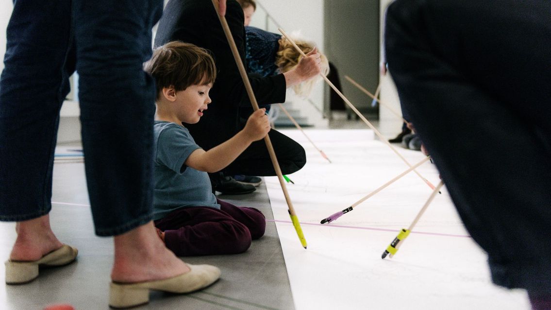 Photo: A child and several adults painting together on the floor.