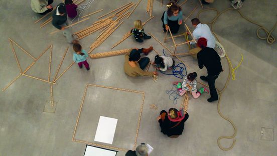 Foto: Erwachsene und Kinder bauen Gebilde aus Holzlatten und Seilen.