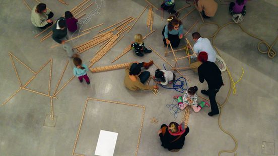 Foto: Erwachsene und Kinder bauen Gebilde aus Holzlatten und Seilen.