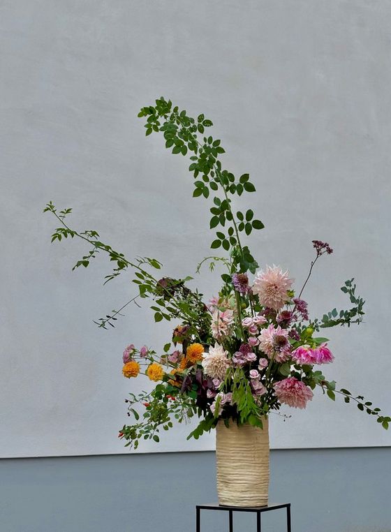 Foto: Ein üppiges Blumenbouquet steht in einer cremefarbenen Vase vor einer hellgrauen Wand.