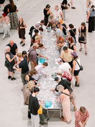 Foto: Eindrücke der Veranstaltung, die entweder Personen um einen langen Tisch mit Klebetattos, im Foyer oder Außenraum der Berlinischen Galerie.