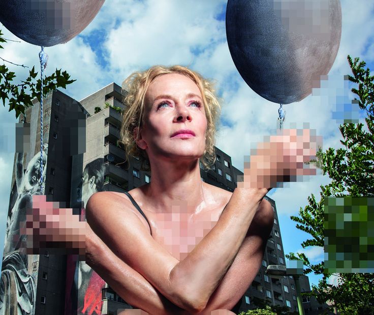 Katja Riemann Foto: Katja Riemann sitzt unbekleidet in der Hocke vor einem Plattenbau und hält jeweils einen gräulichen Luftballon in den Händen. Die Hände, der Brust- und Intimbereich sind verpixelt.
