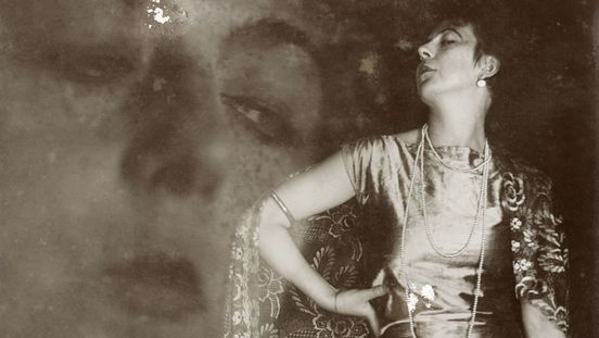 Photograph: The photograph shows the artist in a long satin dress with a long, ornamental train and in a pose. A slightly transparent close-up of her face can be seen in the background.