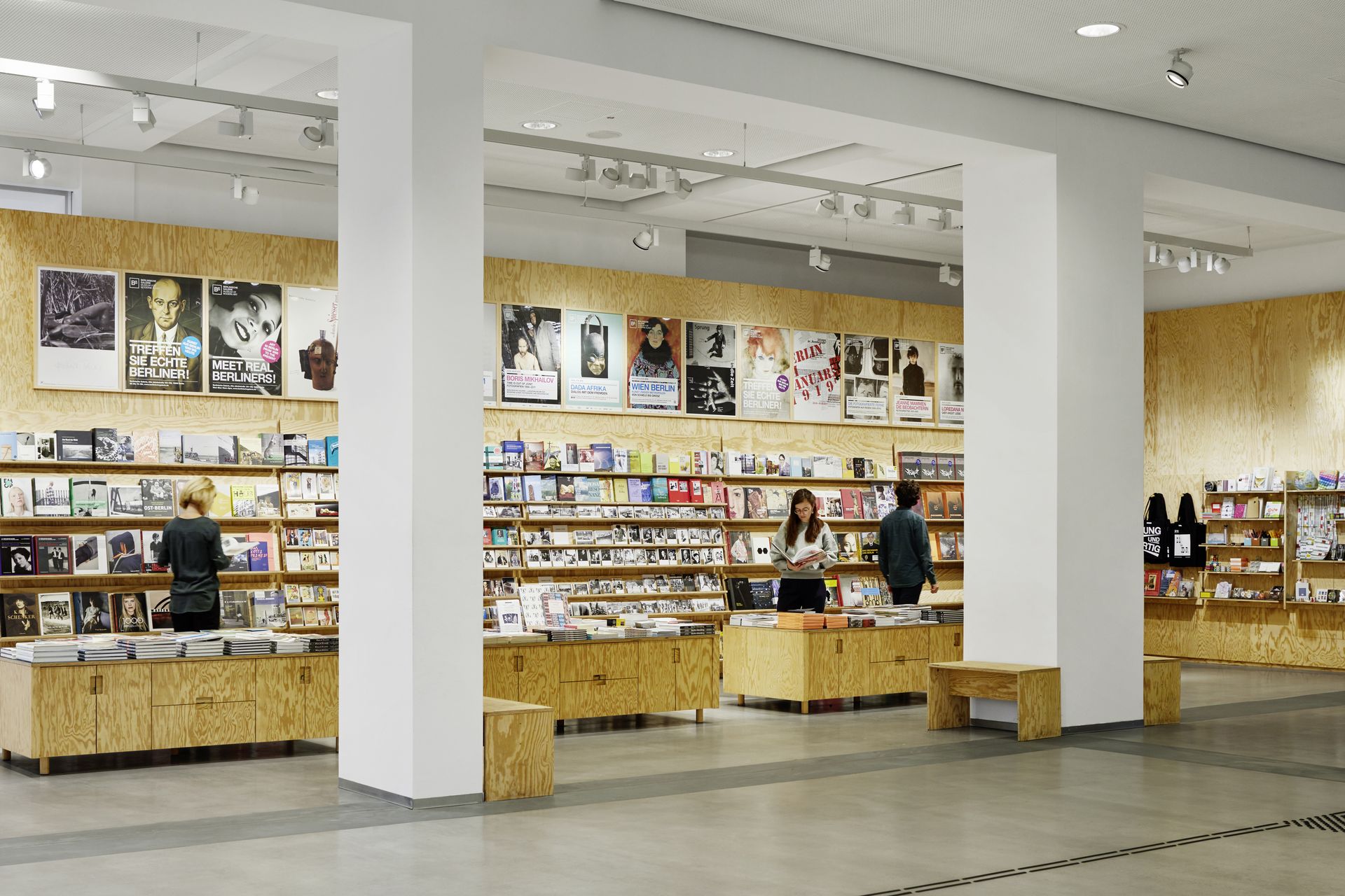 Photo: In the museum shop there are wooden shelves with books, postcards and other products. Several people are looking at them.