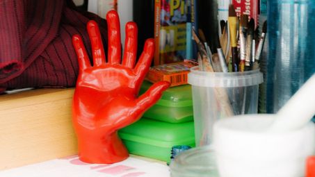 Foto: Ein Regal mit Büchern, Pinseln und weiteren Materialien.